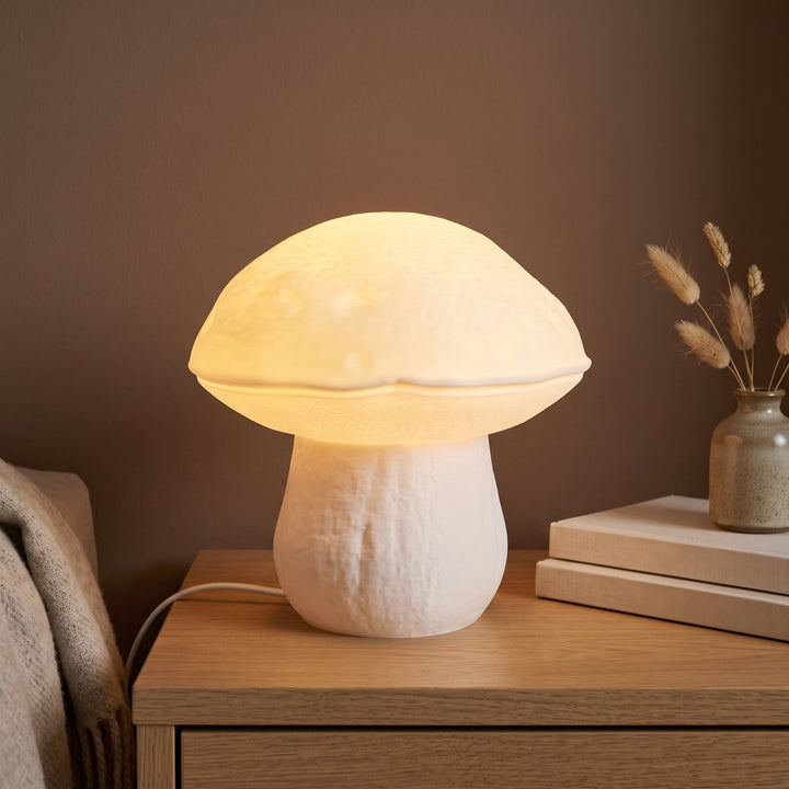 LED Pilzlampe Steinpilz in Weiß, leuchtend auf dem Nachttisch vor brauner Wand