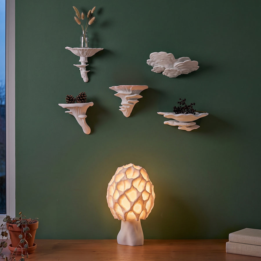 Fünf weiße Pilz-Wandregale an waldgrüner Wand, darunter leuchtet eine weiße Morchel-Pilzlampe auf dem Sideboard.